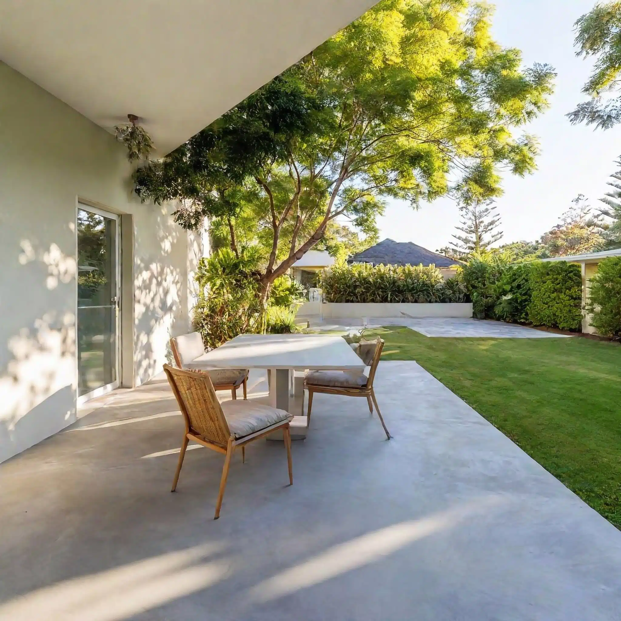 A covered concrete patio with dining furniture in an established garden