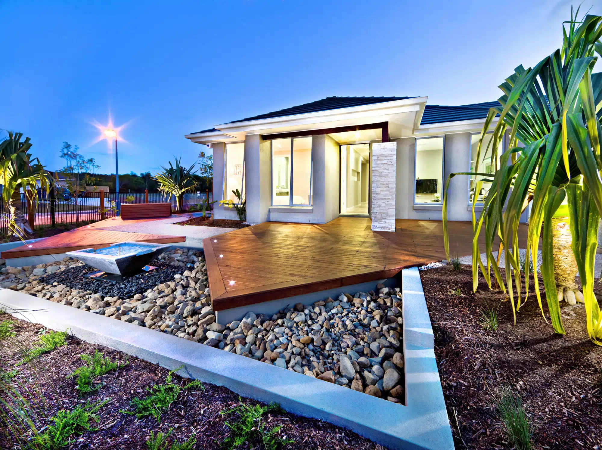 A timber deck at dusk with a stone water feature and garden lighting