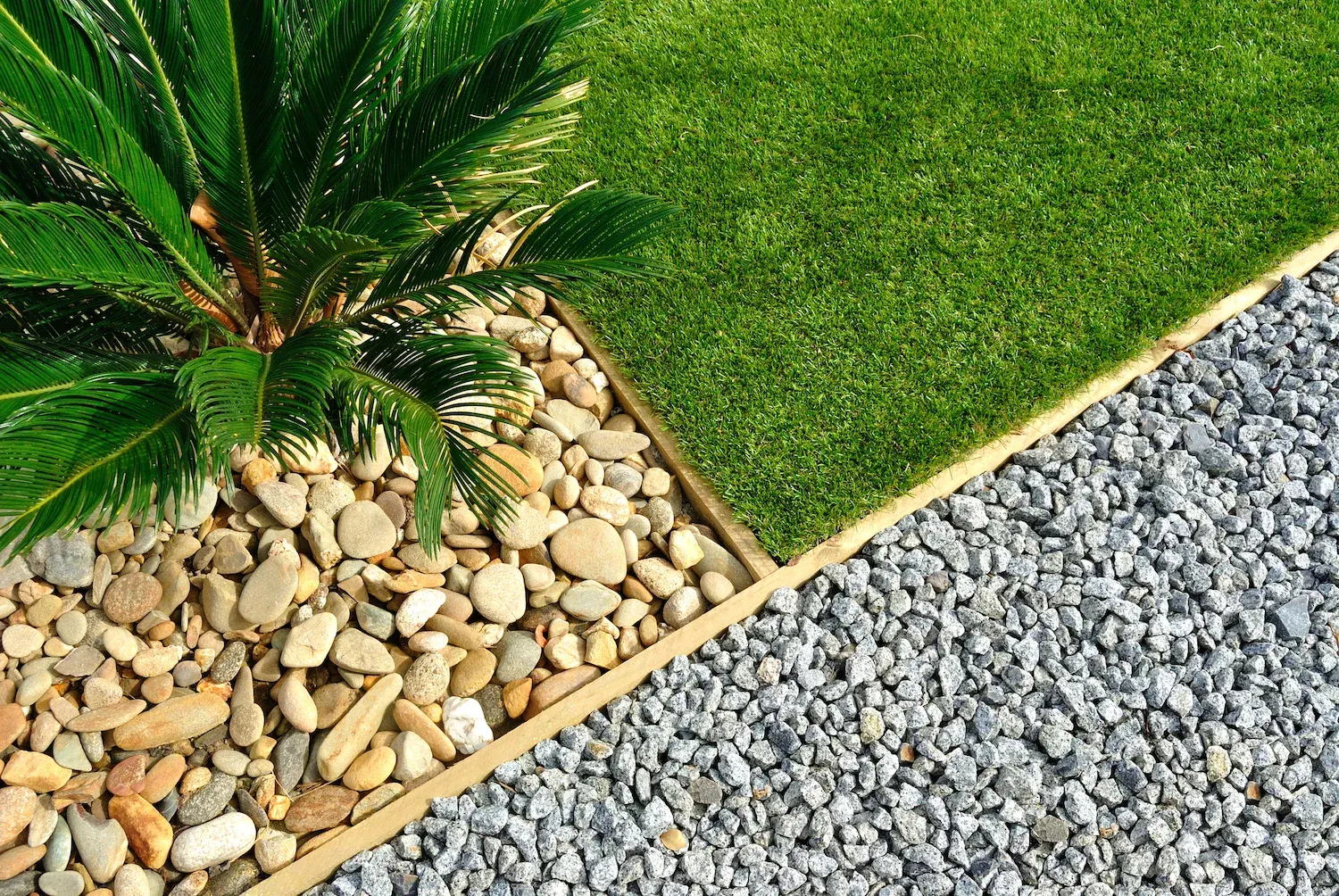 A close-up of a garden edge with turf, pebbles and planting