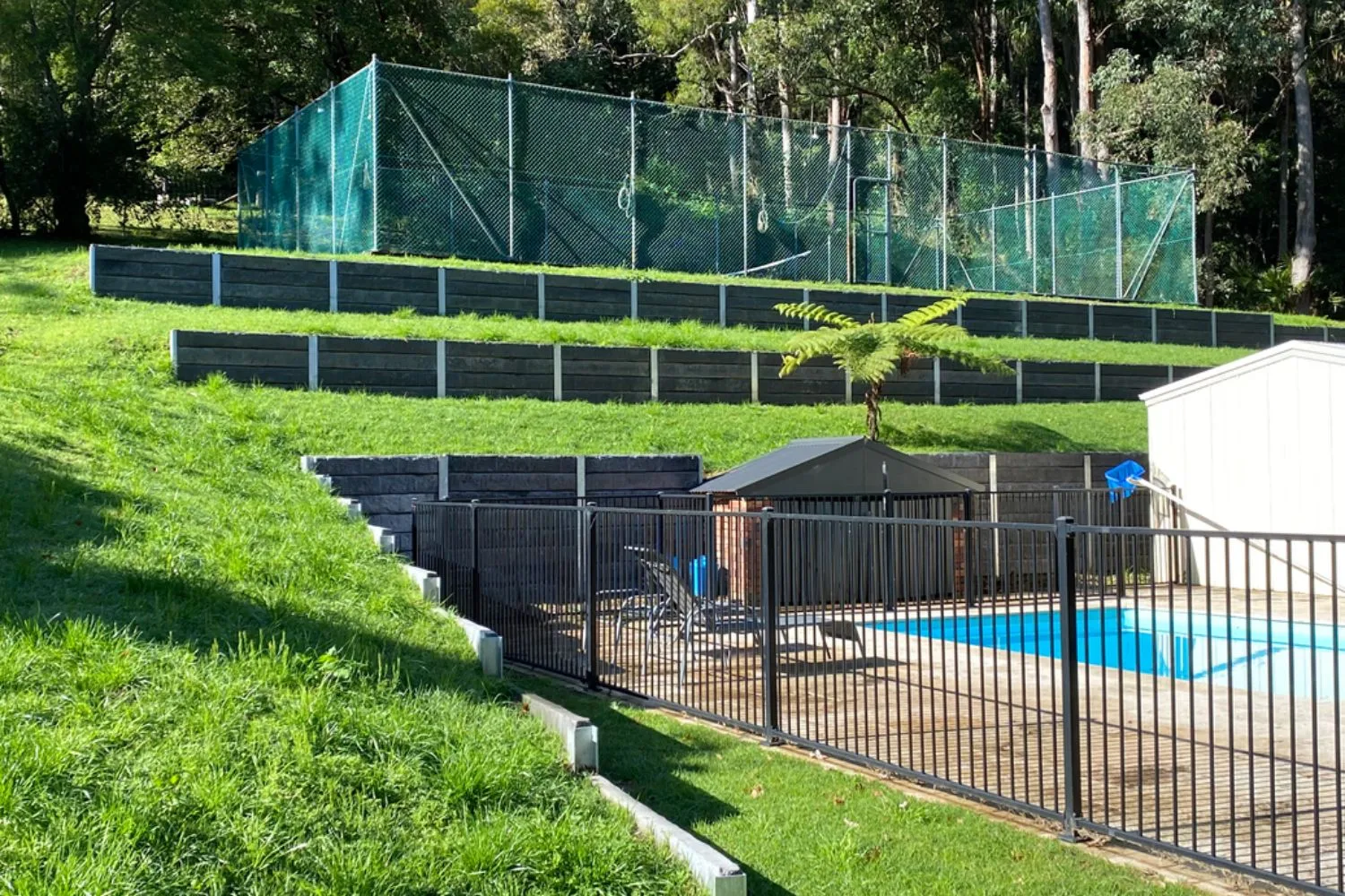 A sloping backyard with terraced concrete sleeper retaining walls leading down to a pool